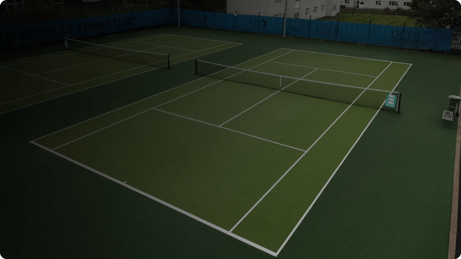 Tennis courts with green surfaces and white lines, surrounded by blue banners and buildings.
