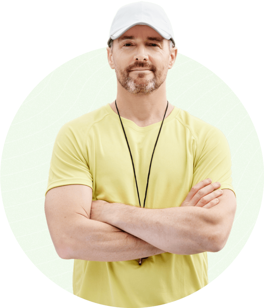 Bearded man in yellow shirt and white cap with arms crossed against green patterned background