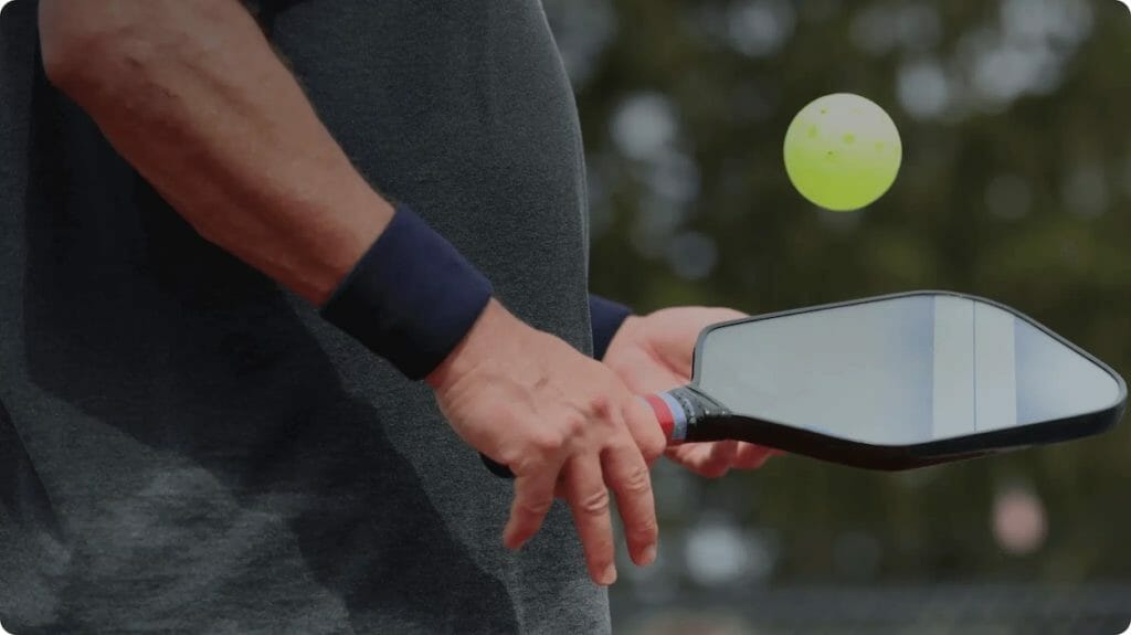 Person playing pickleball, holding a paddle with a yellow ball in the air.