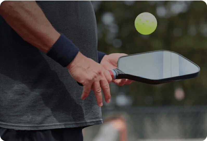 Person holding a pickleball paddle with a ball in the air.