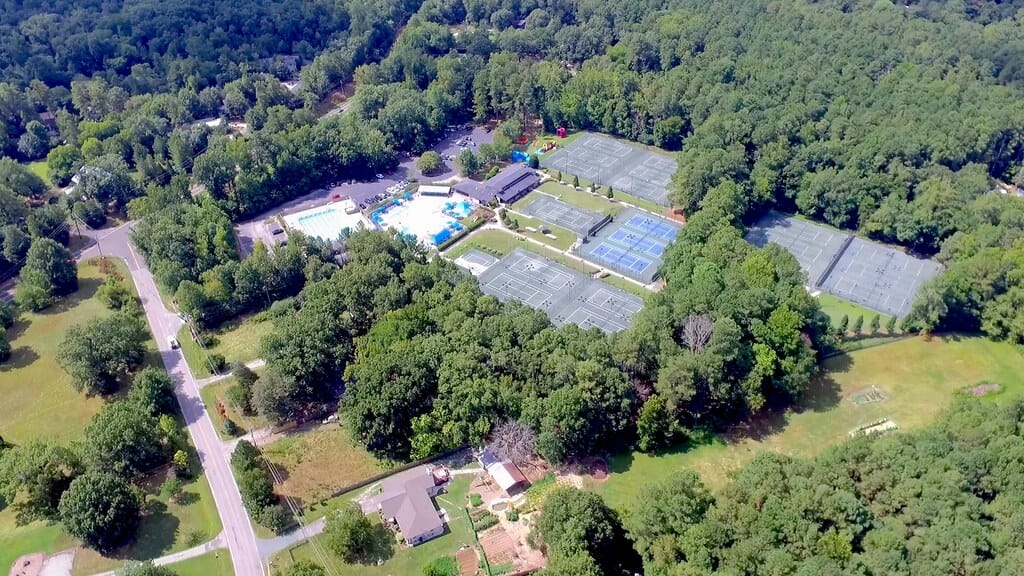 Aerial view of recreational complex in forest with tennis courts, pool area, and buildings.