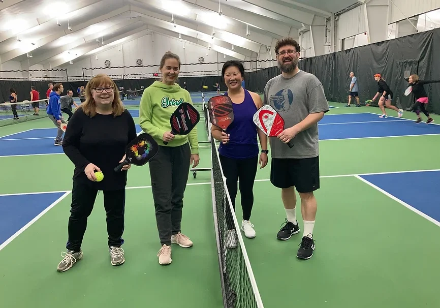 Four people holding pickleball paddles standing on an indoor court.