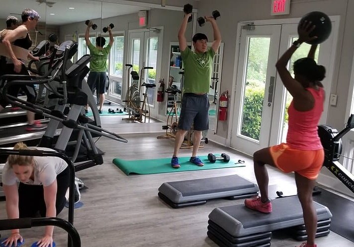 People exercising in a gym with treadmills, weights, and a rowing machine.