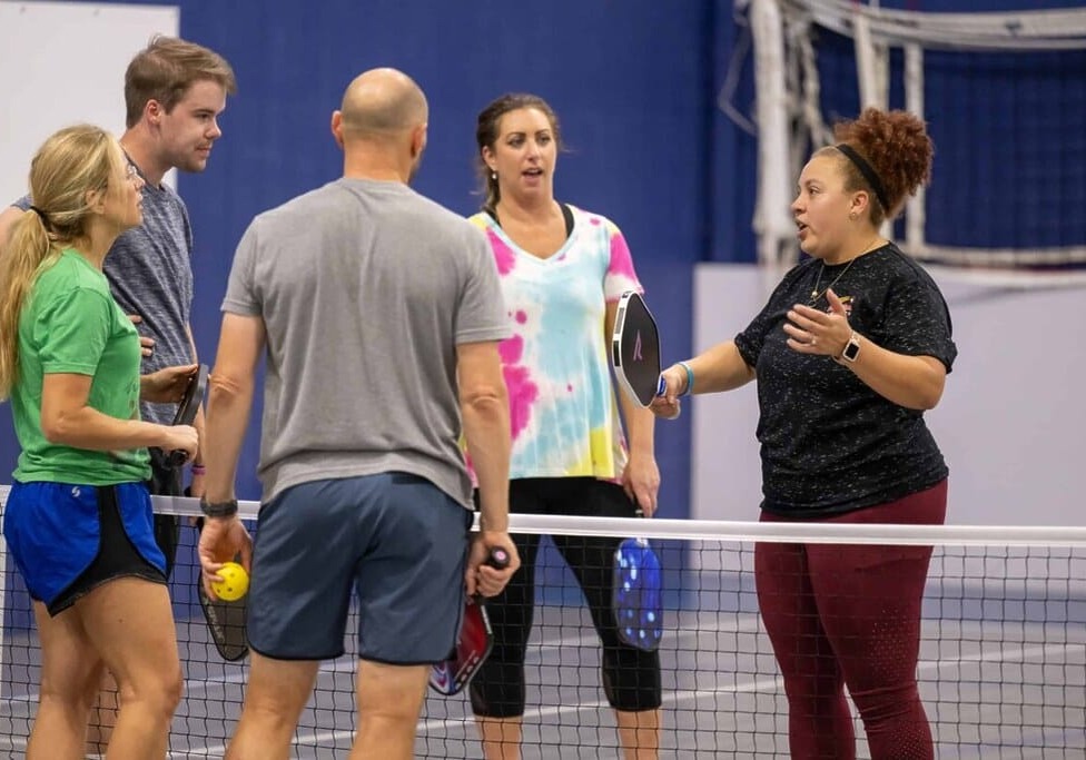 Five people standing on a pickleball court, holding paddles and talking.